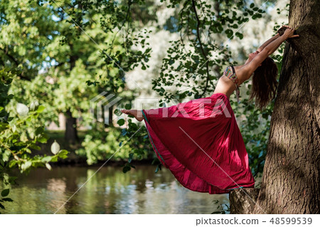 Caucasian woman in forest holding tree doing yoga Caucasian woman in forest holding tree doing yoga 48599539