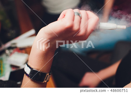 IQOS heat-not-burn tobacco product technology. Woman holding e-cigarette in his hand before smoking. IQOS heat-not-burn tobacco product technology. Woman holding e-cigarette in his hand before smoking. 48600751