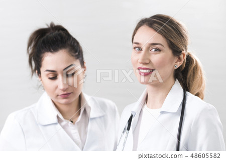 Two female assistants dressed in white coats talking to each other in the dentistry center 48605582