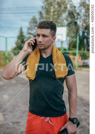 A male athlete holds a phone in his hand, calls on the phone, and rests after a workout in the fresh 48609192