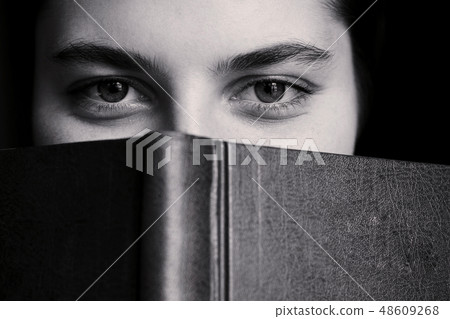 A girl with big eyes hides behind a book. A girl with big eyes hides behind a book. 48609268