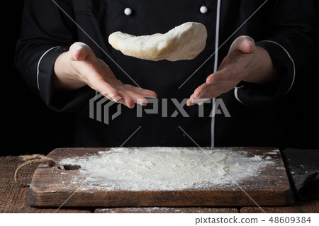 A female cook throws a yeast dough. 48609384