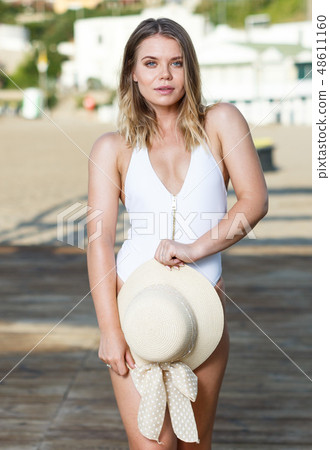 Attractive girl in swimsuit with hat standing near hotel at ocean shore 48611160