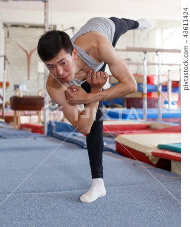 Positive man acrobat exercising gymnastic action at sport gym Positive man acrobat exercising gymnastic action at sport gym 48611424