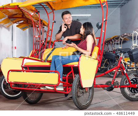 Cheerful girl with boyfriend wanting to hire touristic trishaw for urban trip Cheerful girl with boyfriend wanting to hire touristic trishaw for urban trip 48611449