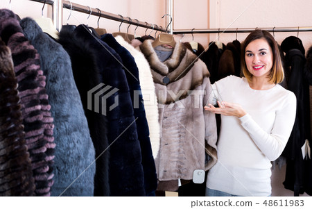 Female customer examining short coffee-colored fur jacket Female customer examining short coffee-colored fur jacket 48611983