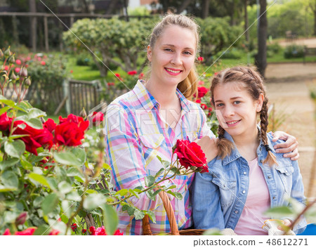 woman and teen holding a basket and standing in the park of roses. woman and teen holding a basket and standing in the park of roses. 48612271