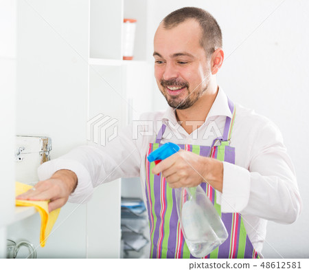 Young man in apron cleaning shelves Young man in apron cleaning shelves 48612581