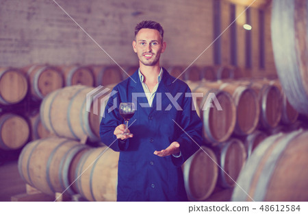 Male winemaker in uniform having glass of wine in hands in cellar Male winemaker in uniform having glass of wine in hands in cellar 48612584