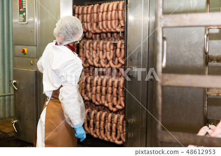 Woman checking sausages in baking machine Woman checking sausages in baking machine 48612953