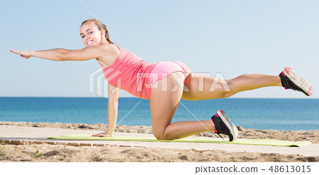 Smiling girl in track-suit practice yoga at sea beach Smiling girl in track-suit practice yoga at sea beach 48613015