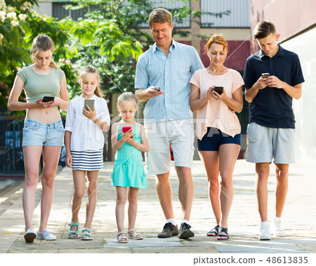 Portrait of smiling large family standing with their mobile phones together outdoors Portrait of smiling large family standing with their mobile phones together outdoors 48613835
