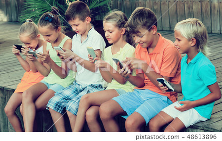Group of kids playing with mobile phones outdoors Group of kids playing with mobile phones outdoors 48613896