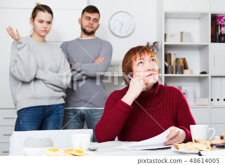 Distressed aged woman with paperwork and irritated family behind Distressed aged woman with paperwork and irritated family behind 48614005