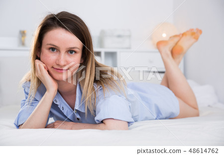Attractive girl in blue shirt lying in bed in home interior Attractive girl in blue shirt lying in bed in home interior 48614762