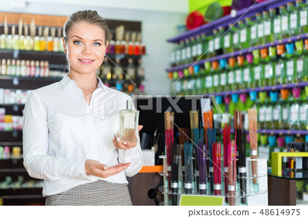 Positive salesgirl suggesting perfume in modern cosmetic store Positive salesgirl suggesting perfume in modern cosmetic store 48614975