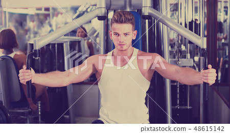 vigorous young man training upper body using fly machine vigorous young man training upper body using fly machine 48615142