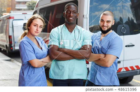 Portrait of three paramedicals in uniform near ambulance car Portrait of three paramedicals in uniform near ambulance car 48615396