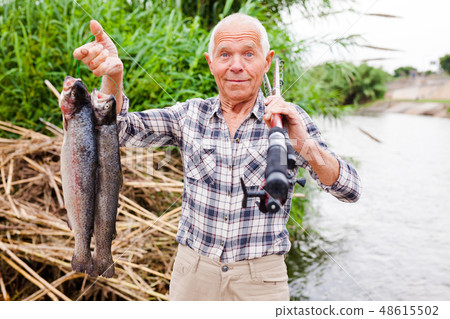 Fisherman posing with catch at riverside Fisherman posing with catch at riverside 48615502