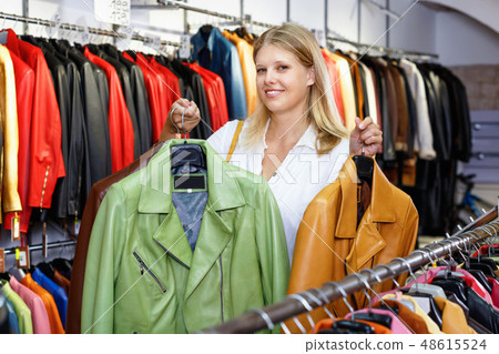 Positive girl looking for new leather jacket during shopping in retail shop 48615524