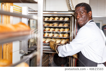 Baker taking out bread from oven 48615583