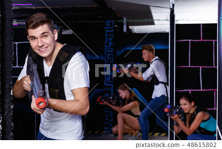 Portrait of excited guy with laser pistol playing laser tag in arena Portrait of excited guy with laser pistol playing laser tag in arena 48615802
