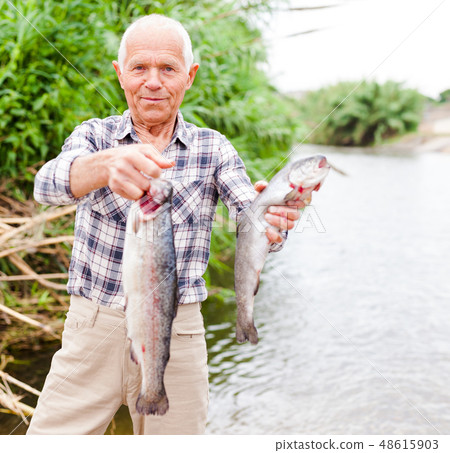 Fisherman posing with catch at riverside Fisherman posing with catch at riverside 48615903