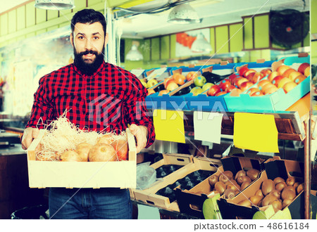 Adult male seller offering pomegranates in shop 48616184