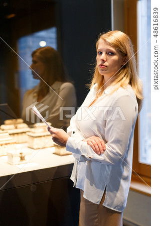 Girl visitor holding guide book standing near art objects in museum Girl visitor holding guide book standing near art objects in museum 48616839
