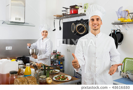 Young cook wearing uniform working on kitchen Young cook wearing uniform working on kitchen 48616880