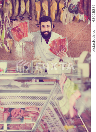 Smiling male seller showing sliced prosciutto Smiling male seller showing sliced prosciutto 48616882