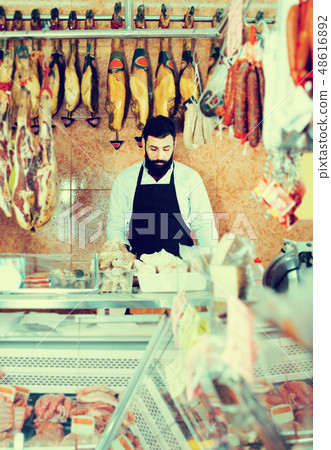 Shop assistant arranging meat to sell in butcher’s shop 48616892