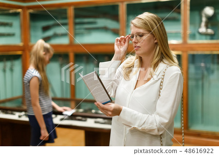 Female holding guidebook in museum of art, daughter on background Female holding guidebook in museum of art, daughter on background 48616922