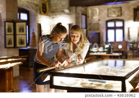 Girl with woman looking with interest at art objects under glass in museum 48616962