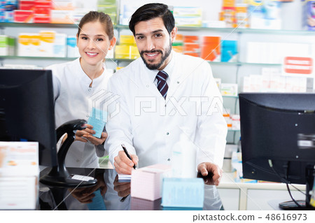 Two pharmacists are attentively stocktaking medicines with computer and note on paper Two pharmacists are attentively stocktaking medicines with computer and note on paper 48616973