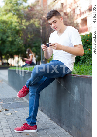 Guy texting on his smartphone in park Guy texting on his smartphone in park 48617053