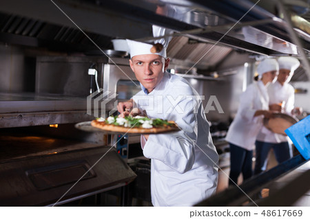 Young chef holding shovel with cooked pizza Young chef holding shovel with cooked pizza 48617669