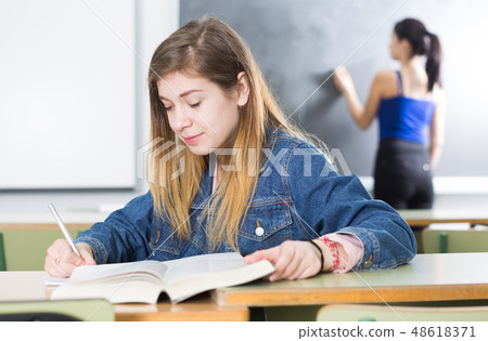 Girl is sitting at the desk and writing homework 48618371