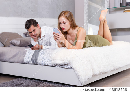 Bored couple with phones on bed Bored couple with phones on bed 48618538