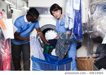 Laundry workers putting clothes in washing machine 48618985