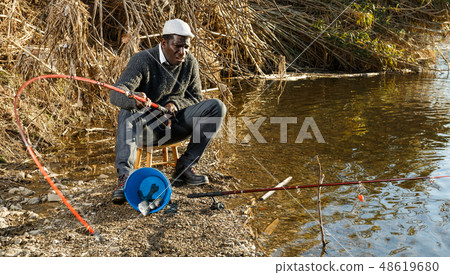 Fisherman sitting on stool and pulling fish Fisherman sitting on stool and pulling fish 48619680