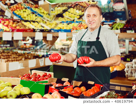 Positive man seller is standing with box with tomatos Positive man seller is standing with box with tomatos 48619794