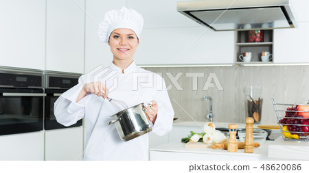 Cheerful woman chef preparing food with whisk on kitchen 48620086