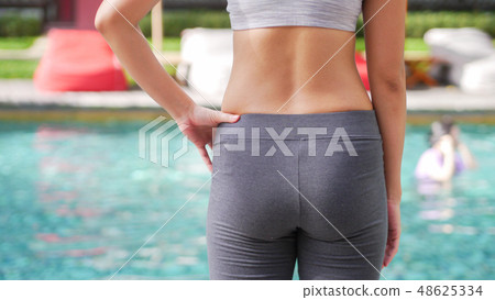 slim woman in yoga sportswear standing beside pool 48625334