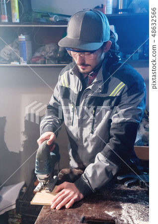 Young man with a beard in gray overalls and goggles by profession a carpenter works as an electric 48632566