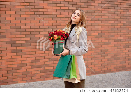 Caucasian fashion woman standing on the street near storefront shop windows holding flower-box with Caucasian fashion woman standing on the street near storefront shop windows holding flower-box with 48632574