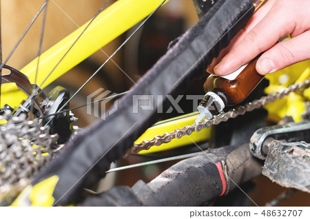 Close-up of a man's hand, led by masters, lubricate the bicycle chain of a mountain bike with a Close-up of a man's hand, led by masters, lubricate the bicycle chain of a mountain bike with a 48632707