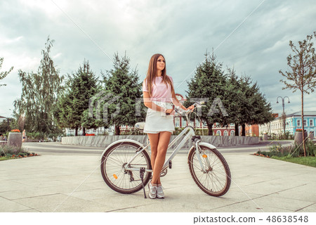 A girl in a white skirt and a pink blouse, stands in summer in the city outdoors on a weekend, a 48638548