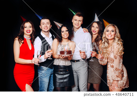 Pretty girl with birthday cake and her friends looking at burning candles at party Pretty girl with birthday cake and her friends looking at burning candles at party 48640711