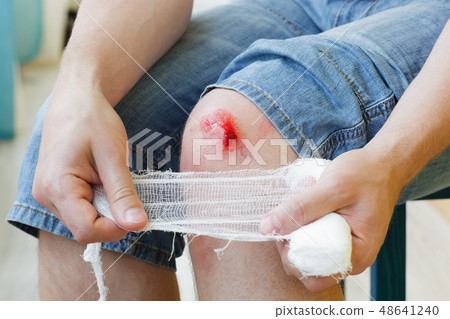 Man heals the wound on his knee at home.  48641240